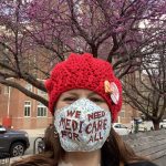 Ops Director Georgia in red beret with We Need Medicare 4 All mask, cherry blossoms behind