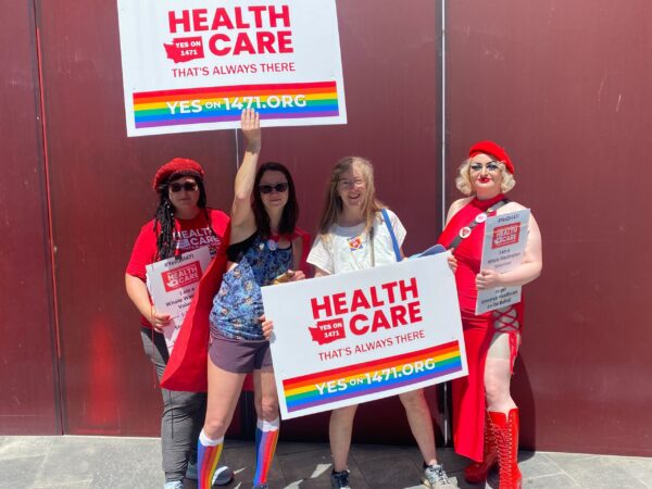 People holding signs that say "healthcare" with rainbow flags.