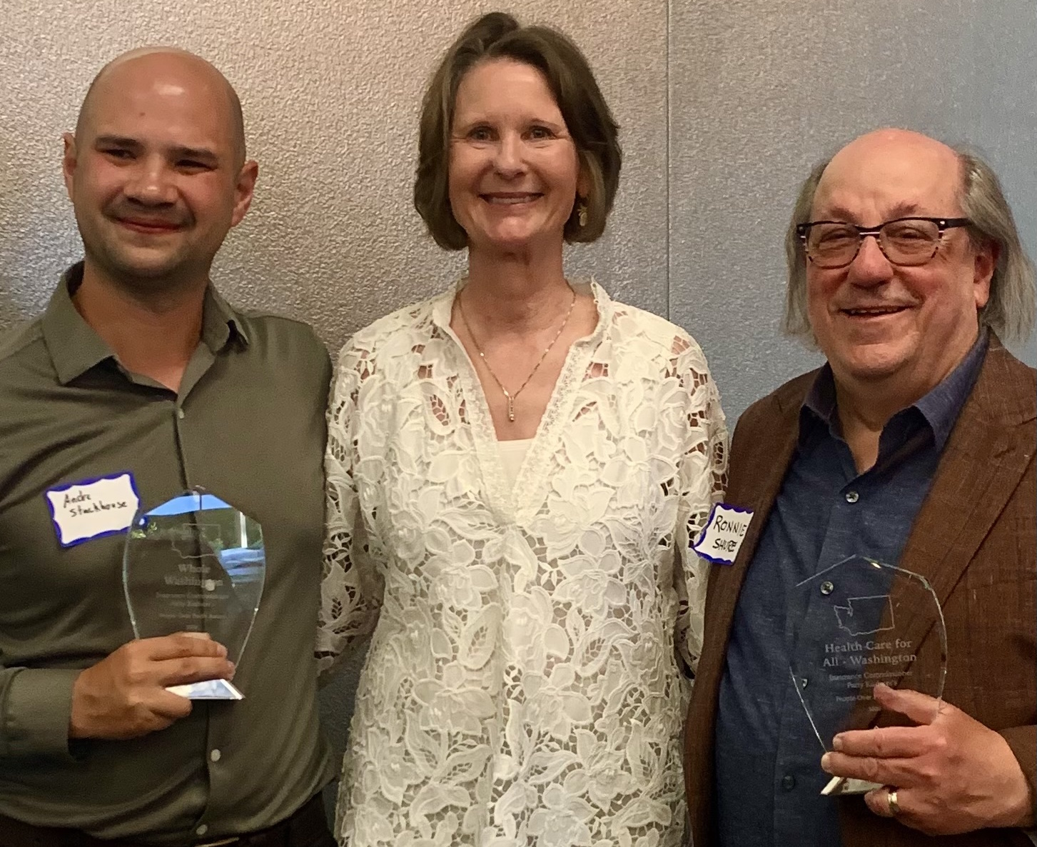 Three people posing, two with awards. Insurance Commissioner Kuderer with Andre Stackhouse (Whole WA executive director) and Ronnie Shure (Health Care for All WA president).